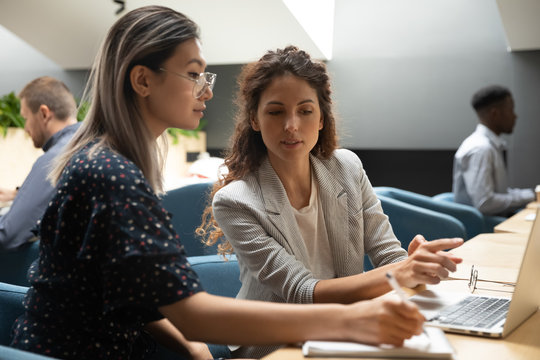 Caucasian female mentor instructing asian trainee explain computer project