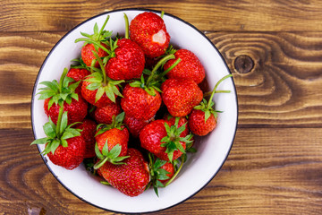 Fresh ripe strawberry in white bowl on a wooden table. Top view