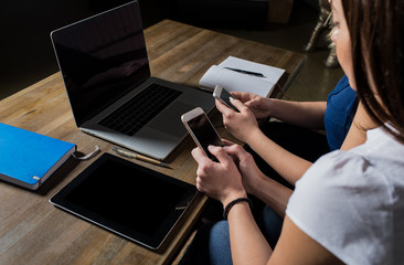 Business persons reading financial news in internet via mobile phones, sitting at the table with open laptop computer and touch pad. Women partner reading text message on website via cell telephones