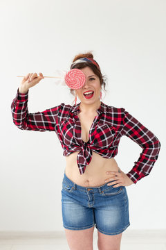 Pretty smiling young woman in a plaid shirt closes her eye with big colorful lollipops and posing against a white background. Concept of fun and desserts.
