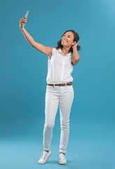 Happy young woman taking selfie on blue background