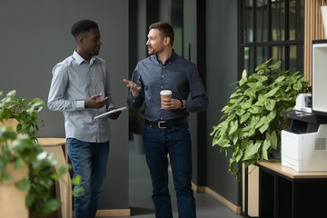 Diverse friendly male partners talking walking in office hallway