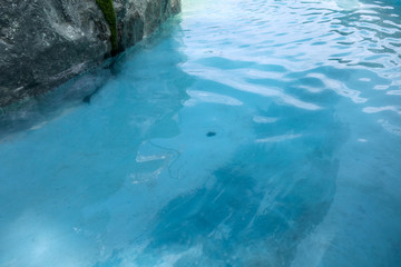 Sea or ocean surface. Sky blue water with small wimples washes black rough rock or stone