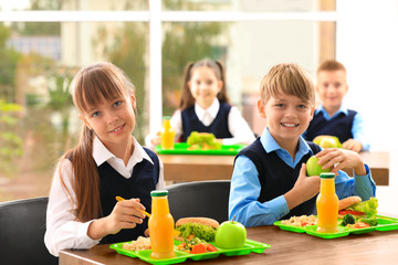 Happy children at table with healthy food in school canteen