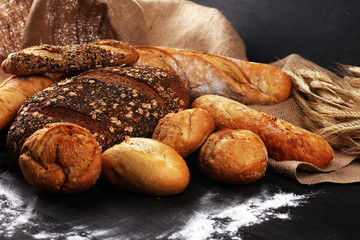 Assortment of baked bread and bread rolls on black table background