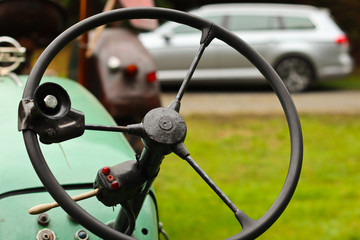 Steering wheel of an old tractor close-up on a background of a modern car