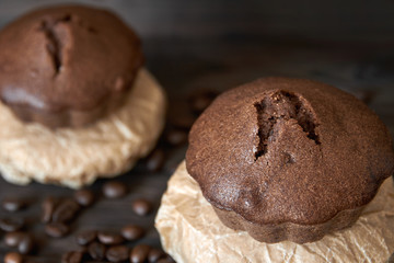Two homemade chocolate muffins on parchment with coffee beans. Dark wooden background, closeup, selective focus