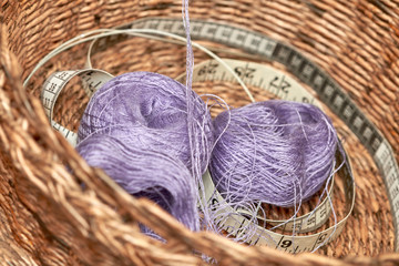 Brown wicker basket from newspaper tubules with two blue knitting balls, needles and meter. Closeup, selective focus