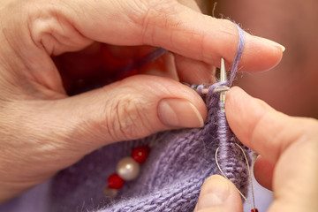 Woman is knitting a blue warm sweater. A hobby of elderly woman is knitting. Closeup view of knitting loop. Selective focus
