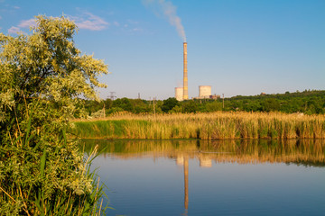 Cogeneration plant (combined heat and power station). Thermal power plant with flue pipe. Industrial landscape with water, trees and power lines