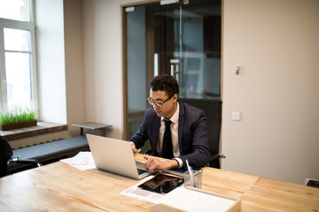 Man professional economist searching information in internet on laptop computer while sitting in modern office. Male intelligent employee using applications on notebook during work day in company
