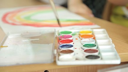 The child draws blue paint on a brush for painting. The artist s children's hand draws paint on the brush. Children draw rainbows in an educational institution. Child's hand with a brush closeup.