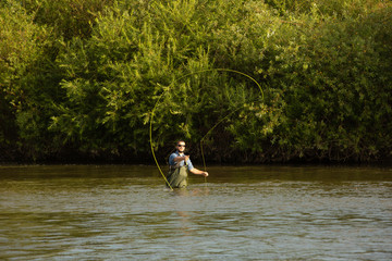 The fisherman stands at waist-deep in water. A man in a special waterproof suit throws a fishing rod