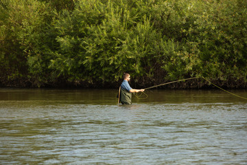 The fisherman stands at waist-deep in water. A man in a special waterproof suit throws a fishing rod