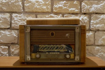 Retro wooden and rusty old radio receiver on a wooden table indoors used for decoration. Background view of blurred, not in focus, stone wall