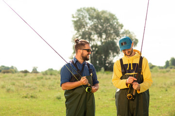 Two fishermen preparing for fishing. They hold the fishing rods and talk to each other. Sport fishing