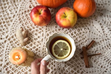 Hand taking cup of warm tea with lemon with pumpkins, apples, candle and spices, fall scene