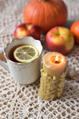 Cup of warm tea with lemon with pumpkins, apples, candle and spices, fall scene