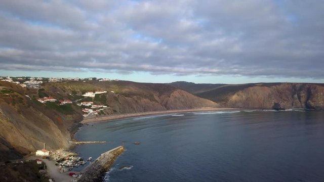 Aerial, reverse, drone shot, over a couple taking pictures, on a cliff, at the Arrifana Beach, at the Atlantic shore, on a sunny day, in Vicentina coast national park, Aljezur, Portugal
