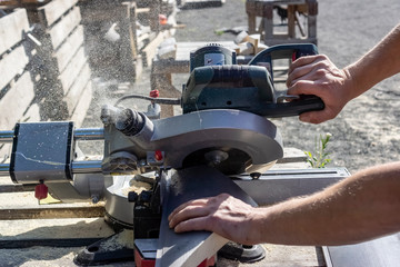A carpenter saws off a board with a circular saw - obrazy, fototapety, plakaty