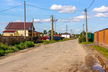 Fototapeta na wymiar Country road between low-rise houses in village in summer