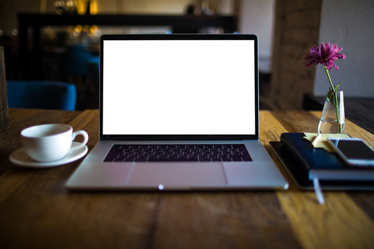 Modern laptop computer with white blank monitor background with copy space for promotional content lying on a coffee shop table near cup of tea and notebook. Open netbook with empty screen