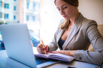 Female smart government organisation writing information in diary during work on laptop computer...
