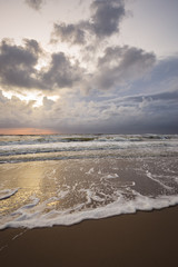 Vertical view of the coast with clouds over sea at sunset. Beautiful reflections in the water at the beach.