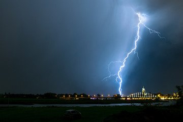 Forked lightning strikes down from a thunderstorm close to a bridge in a city.