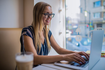Happy smiling woman marketing coordinator keyboarding promotional content on web page via laptop...