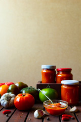 Homemade hot tomato sauce adjika in jars - Tomatoes, chilli pepper, garlic, herbs on wooden table.