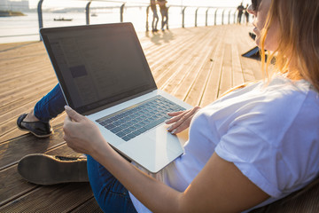 Woman blogger reading article on web page via laptop computer while relaxing on embankment in sunny summer day. Hipster girl skilled freelancer checking e-mail on notebook during rest outdoors
