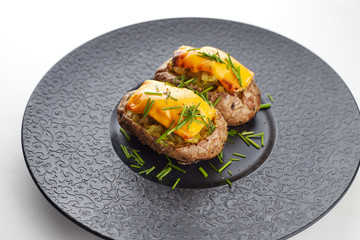 Baked potato with cheese and herbares, on a black plate