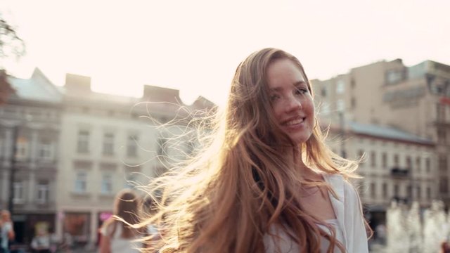 Attactive young smiling woman with curly hair returns look at camera smile walking in the city streets portrait happy summer face sunset beautiful lady outdoor close up slow motion