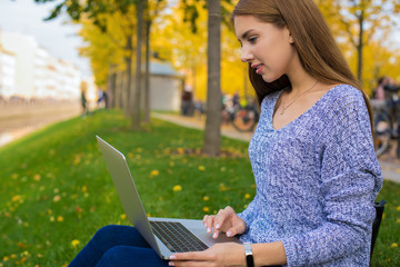 Lovely woman in casual wear professional content manager checks the job of remote workers via laptop computer while sitting in park in autumn day. Pretty female student online learning via notebook