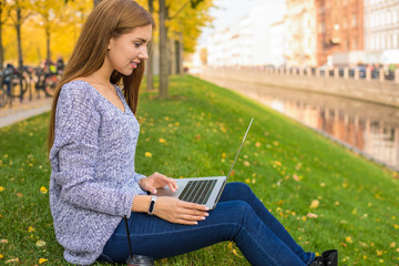 Young gorgeous caucasian woman skilled content creator working distance via laptop computer while resting in park near embankment river background with copy space. Female using applications on netbook