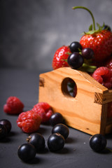 Different berries: strawberries, cherries, raspberries, currant in a wooden basket on a gray background
