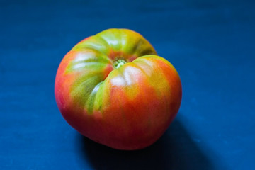 Large red-green unripe tomato on a blue background.