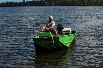 Fototapeta na wymiar Older gray haired man in his bright green fishing boat enjoying a sunny summer weekend on the Mattaponi River in Virginia United States
