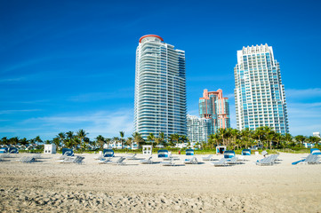 Fototapeta na wymiar Bright scenic morning view of the Miami skyline with lounge chairs waiting for sunbathers on the shore of South Beach at South Pointe