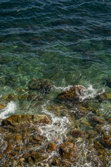 Top view on the sea near coast with waves and crystal clear water. Waves broken by rocks. Vertical line