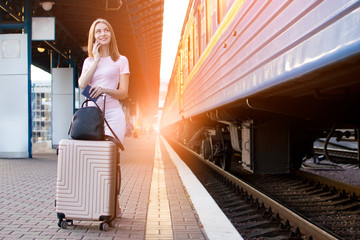 girl stands on the platform of the station with a suitcase and waits for a train, a student travels, leaves for summer vacation, copy space