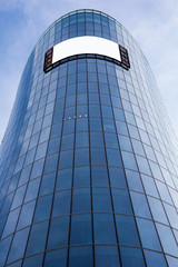 Obraz premium Bottom view of a modern skyscraper building with advertising board with empty mock up screen background for your promotional content. Business centre exterior with blank monitor in urban district