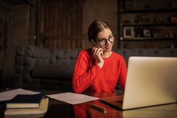 Smiling woman in stylish warm sweater skilled copywriter talking via cell telephone during distance...