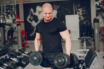 Fototapeta na wymiar A young and muscular guy in a black t-shirt trains in a gym