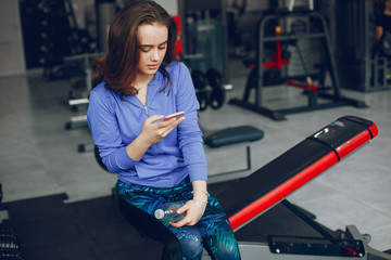 A young and beautiful girl sitting in a gym with phone and water