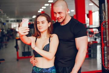 A young and beautiful girl with her boyfriend standing in a gym and use the phone