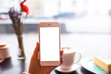 Closely hipster girl holding modern white mobile phone with blank display with copy space background for promotional content while sitting in coffee shop with cup of latte during recreation time