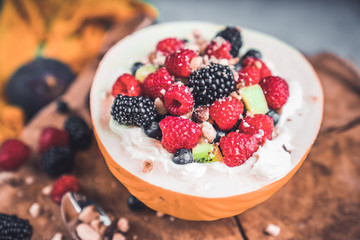  A delicious bowl of melon fruit with a creamy bottom and mixed fruits: raspberries, blueberries, blackberries and kiwi as well as figs. Fruit bowl on wooden tray. Healthy breakfast.