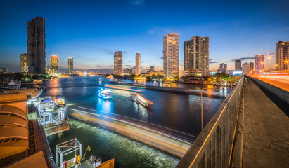 Skyscrapers and Light Trails of Busy Traffic on the Chao Phraya River in Bangkok, Thailand as Seen from Taksin Bridge at Twilight
